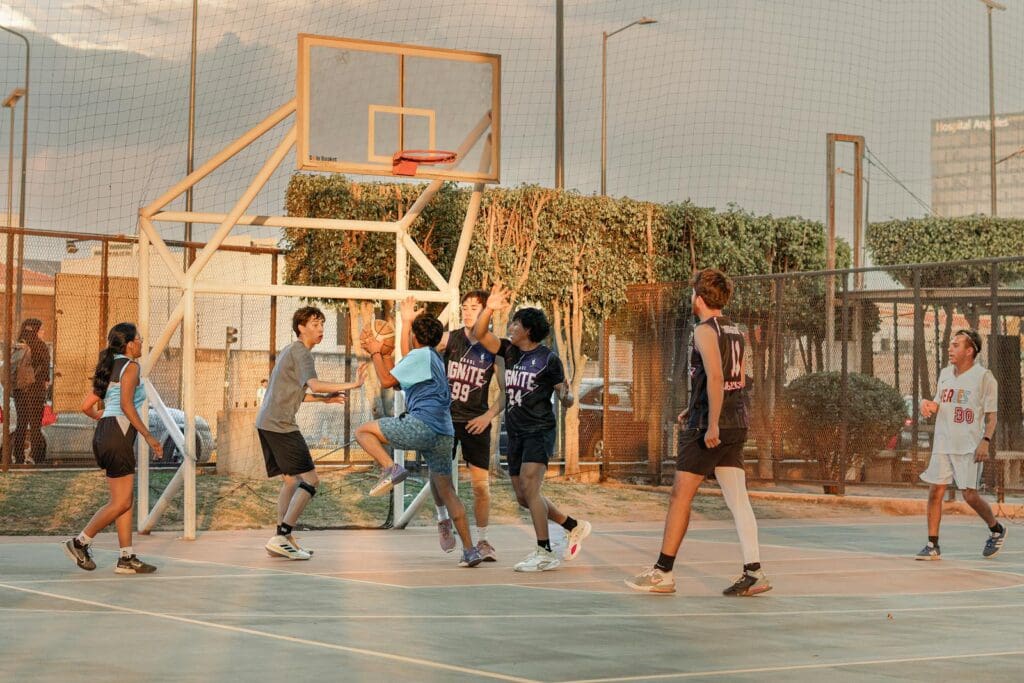 A group of teenagers playing an energetic street basketball game on an outdoor court.