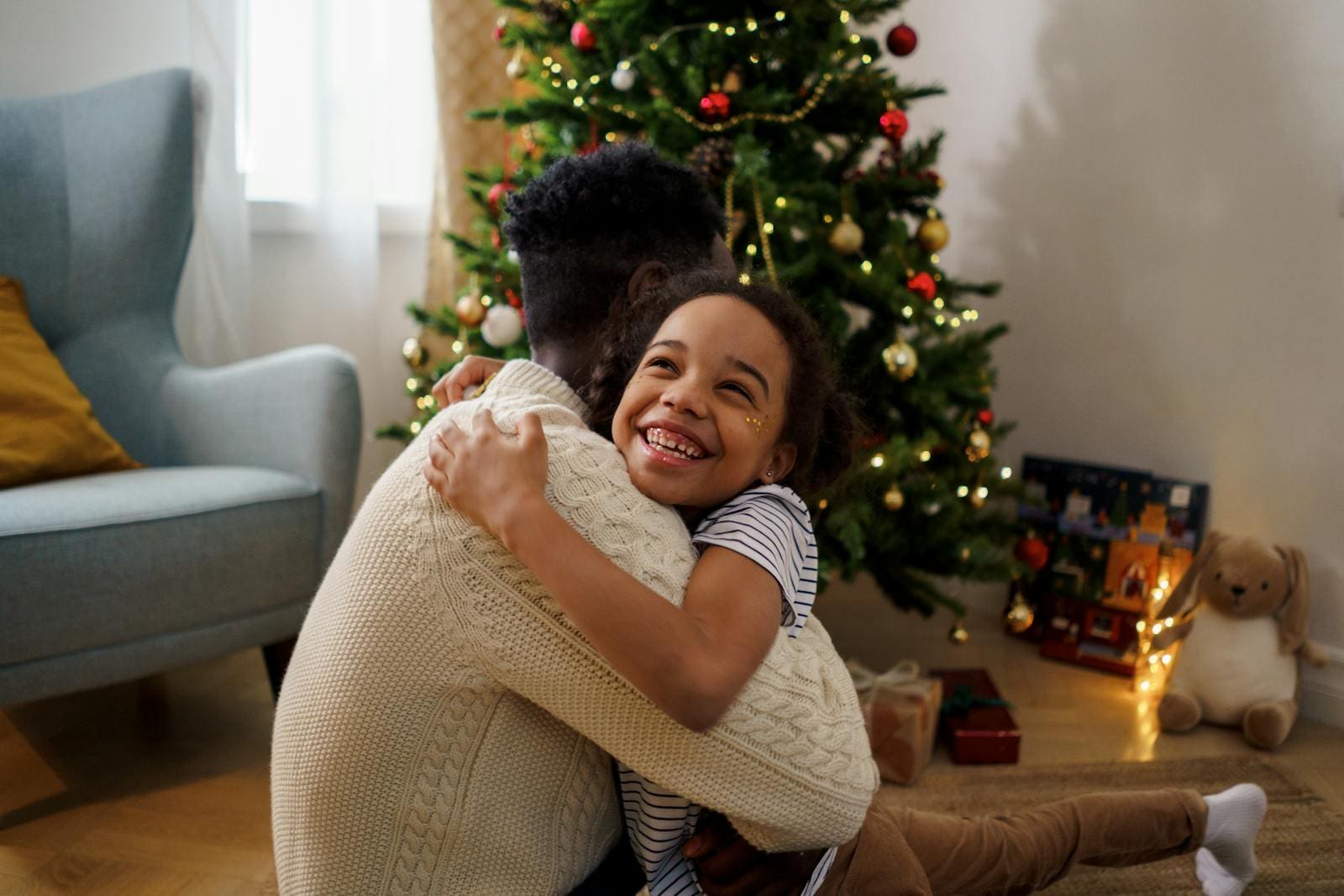 Joyful father and daughter share a warm hug by the Christmas tree indoors during the holiday season.