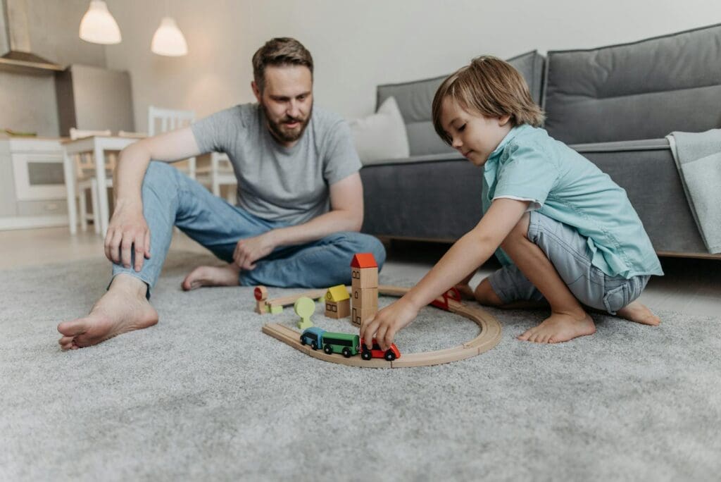 A father and son bond through playtime on the living room floor, enjoying wooden toys.