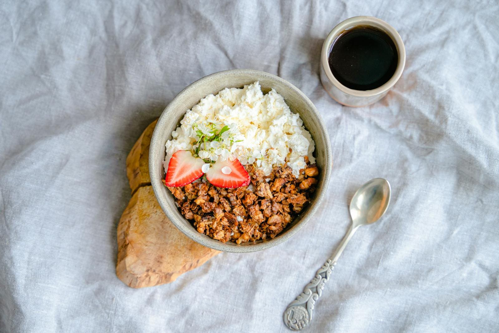 A delicious breakfast bowl with cottage cheese, granola, and strawberries served with black coffee.