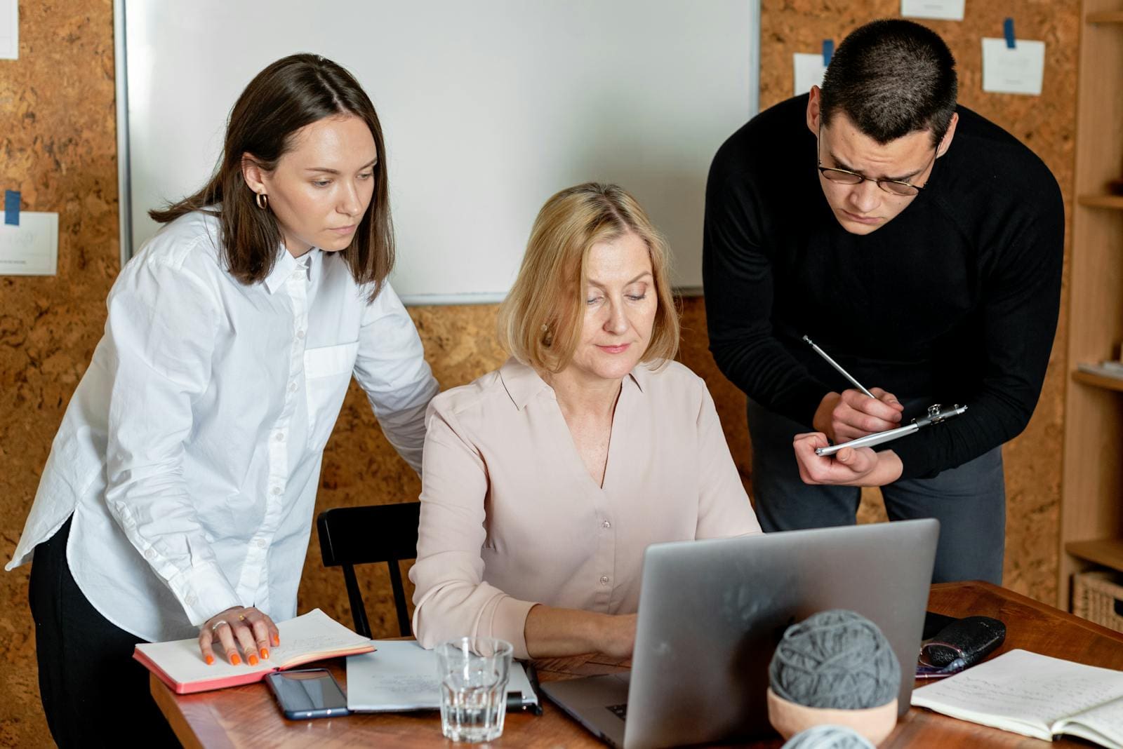 A focused group of professionals collaborating on a project around a laptop in a modern office setting.