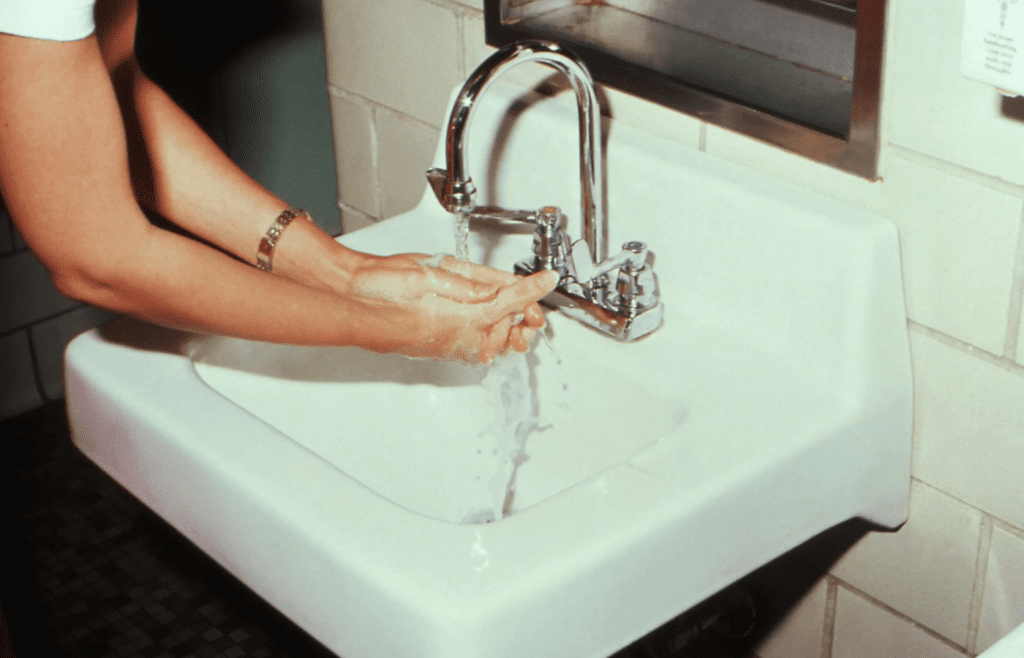 Person washing hands at public restroom sink
