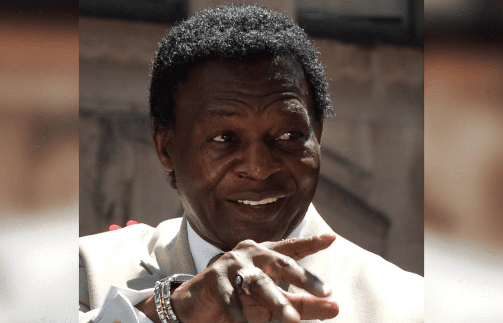 Smiling Lou Brock pointing, wearing suit