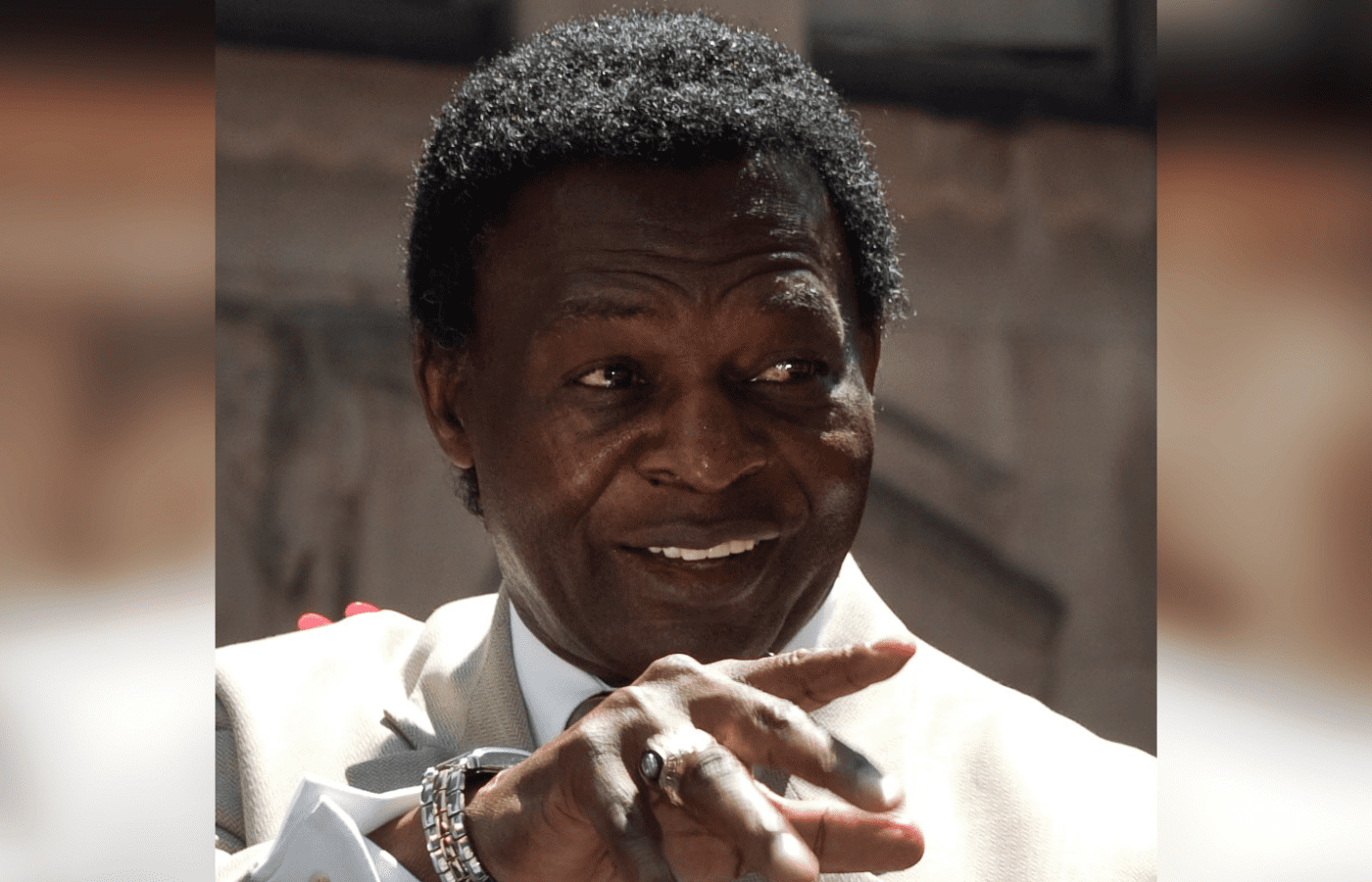 Smiling Lou Brock pointing, wearing suit
