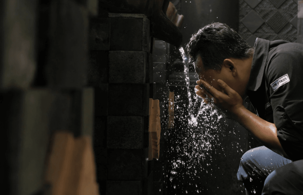 A person splashing water on their face in a bathroom