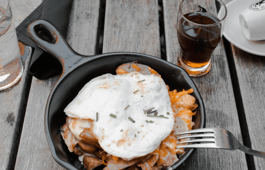 A cast-iron skillet with eggs, bacon, and potatoes sizzling over a fire