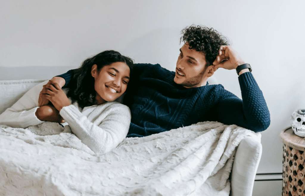 A couple cuddled up on the couch, smiling