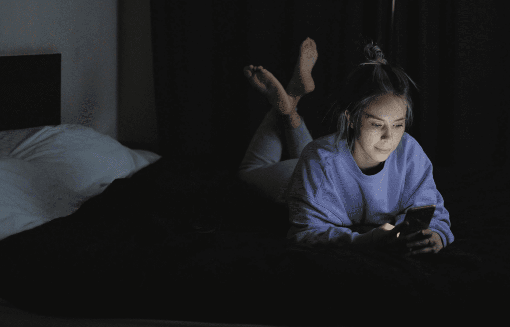 A person lying in bed with their phone glowing in the dark