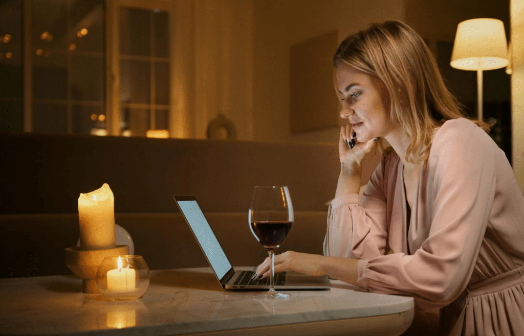 A person shopping online late at night with a glass of wine