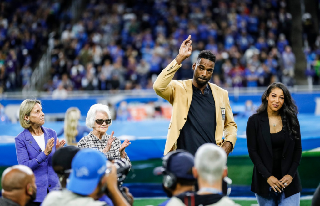 Calvin Johnson waves to Detroit Lions fans as Sheila Ford Hamp, far left, and Martha Firestone Ford, left, clap during Johnson's Hall of Fame Ring Ceremony at Ford Field in Detroit on Sunday, Sept. 26, 2021. At right is Johnson's wife, Brittney