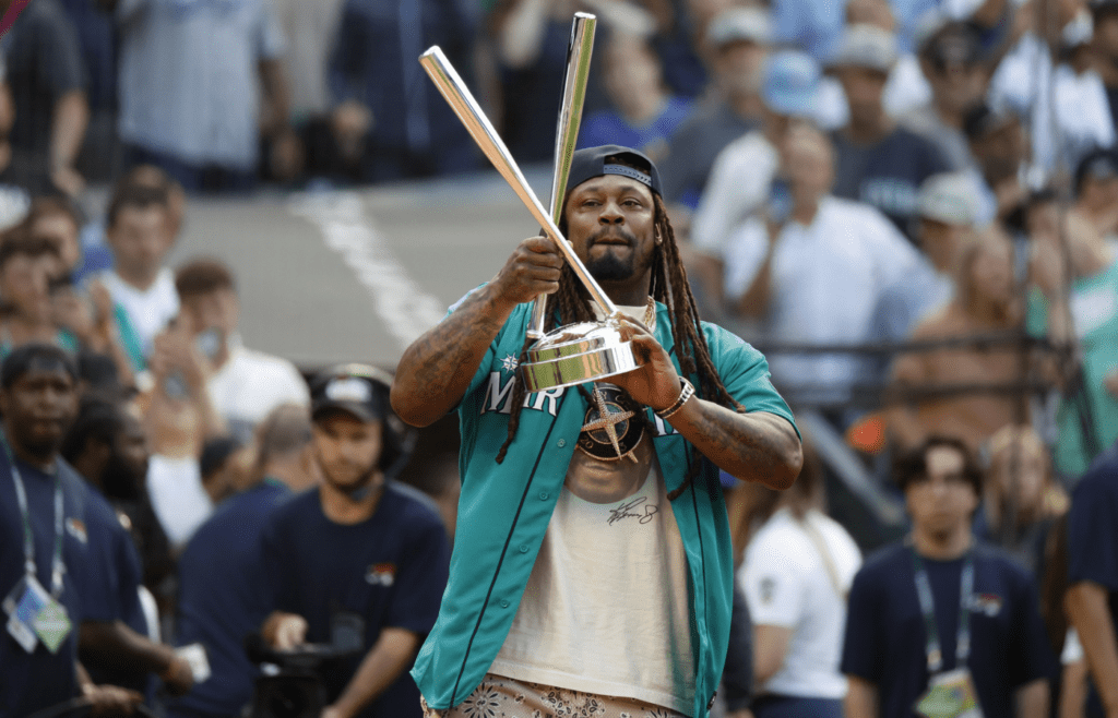 Jul 10, 2023; Seattle, Washington, USA; Former Seattle Seahawks running back Marshawn Lynch brings the championship trophy to the field before the finals of the All-Star Home Run Derby at T-Mobile Park. Mandatory Credit: Joe Nicholson-Imagn Images