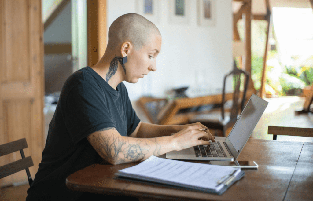 A young professional with visible tattoos typing on a laptop