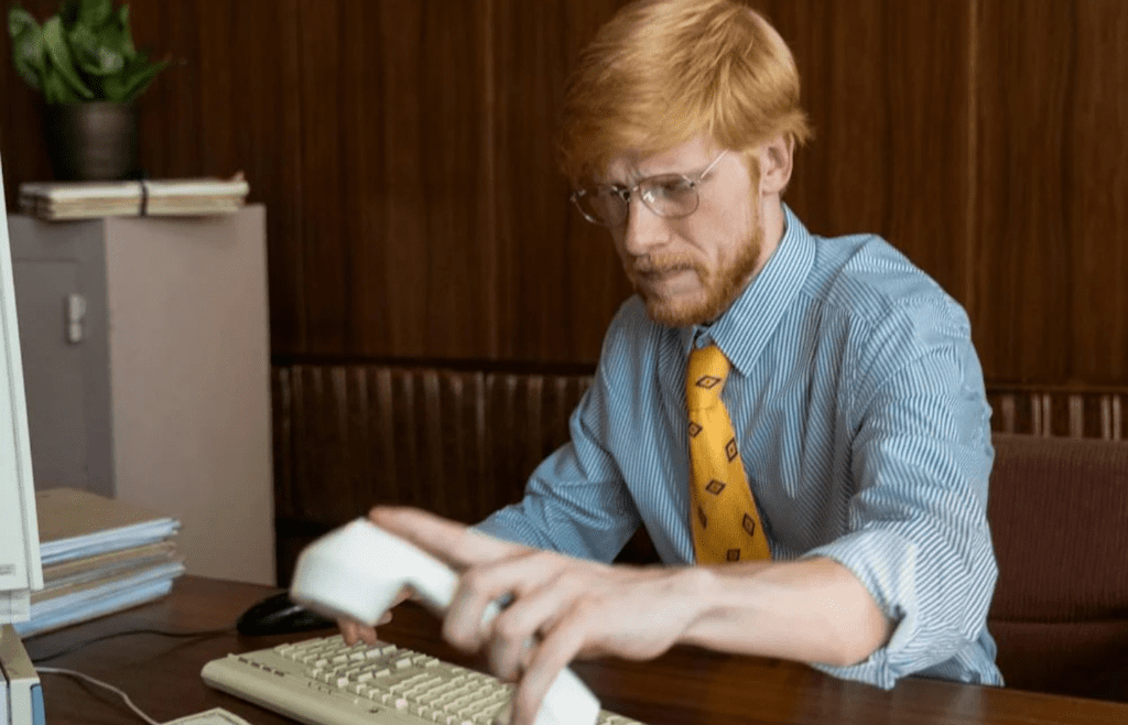 A person sitting at an old computer with a phone cord plugged in