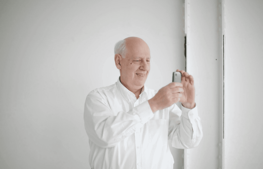 Cheerful bald man taking photo on smartphone