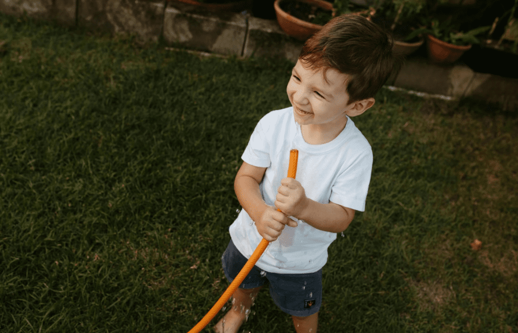 A kid sipping from a green garden hose outside