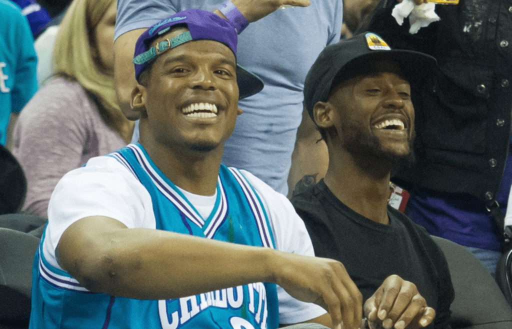 Nov 27, 2015; Charlotte, NC, USA; Carolina Panthers quarterback Cam Newton (L) smiles during the game between the Charlotte Hornets and the Cleveland Cavaliers at Time Warner Cable Arena. The Cavaliers won 95-90. Mandatory Credit: Jeremy Brevard-Imagn Images