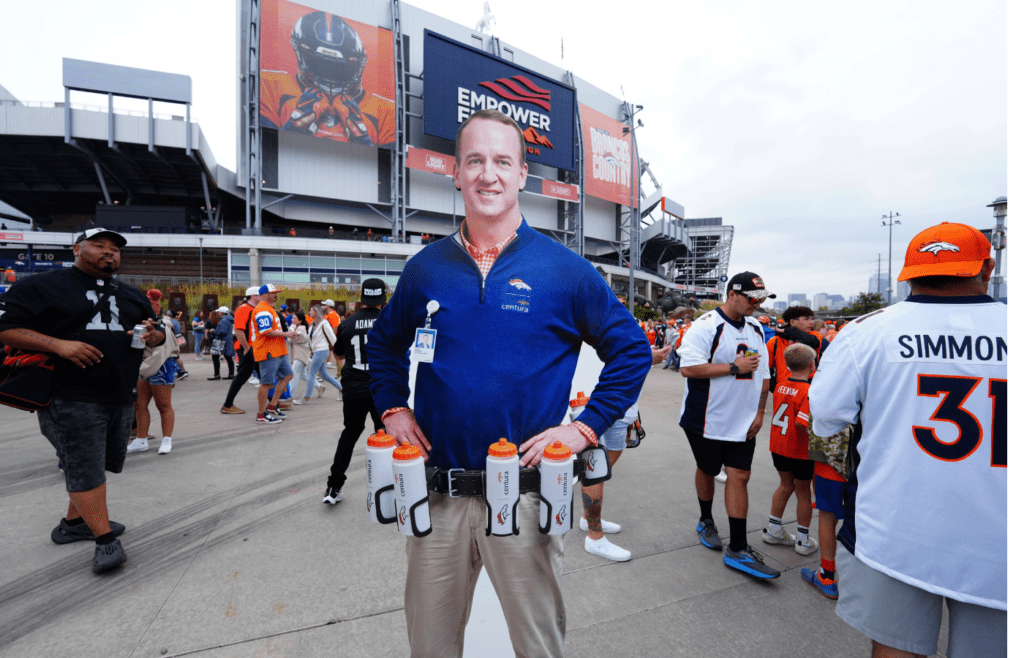 Sep 10, 2023; Denver, Colorado, USA; A cutout of retired NFL football player Peyton Manning stands with fans of the Las Vegas Raiders and the Denver Broncos outside Empower Field at Mile High. Mandatory Credit: Ron Chenoy-Imagn Images