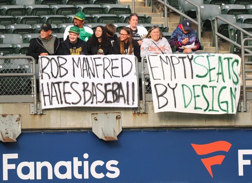 Jun 19, 2024; Oakland, California, USA; Oakland Athletics fans hold signs reading “Rob Manfred hates baseball” and “empty seats by design” during the first inning against the Kansas City Royals at Oakland-Alameda County Coliseum. Mandatory Credit: Kelley L Cox-USA TODAY Sports
