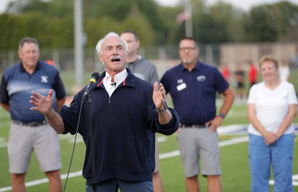 Rocky Bleier speaks to the crowd in regards to the new turf field prior to the Xavier High School football game against Valders Friday, August 23, 2024, in Appleton, Wisconsin. Xavier won 56-12.