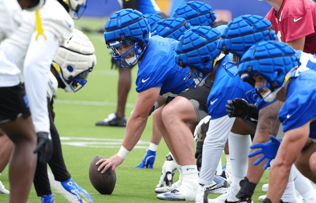 May 28, 2025; Woodland Hills, CA, USA; A general view of the line of scrimmage as Los Angeles Rams center Coleman Shelton (65) takes the snap wearing a Guardian helmet cap during organized team activities at Rams Practice Facility. Mandatory Credit: Kirby Lee-Imagn Images