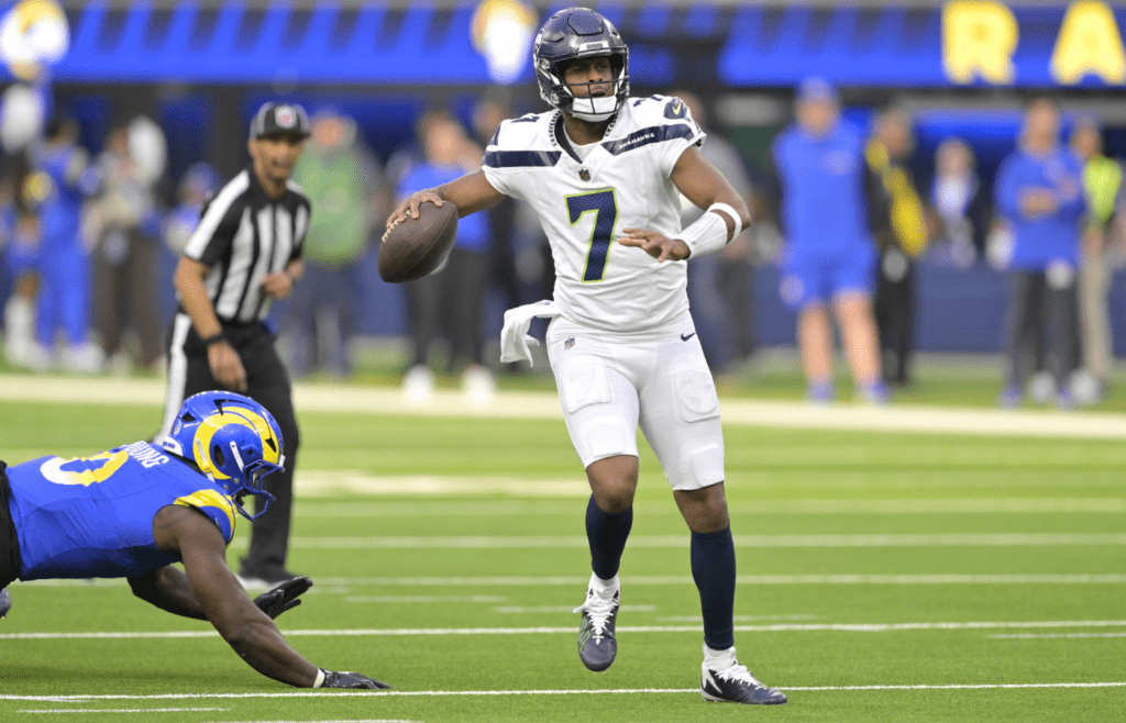 Jan 5, 2025; Inglewood, California, USA; Seattle Seahawks quarterback Geno Smith (7) scrambles away from Los Angeles Rams linebacker Byron Young (0) and throws for a touchdown in the first half at SoFi Stadium. Mandatory Credit: Jayne Kamin-Oncea-Imagn Images