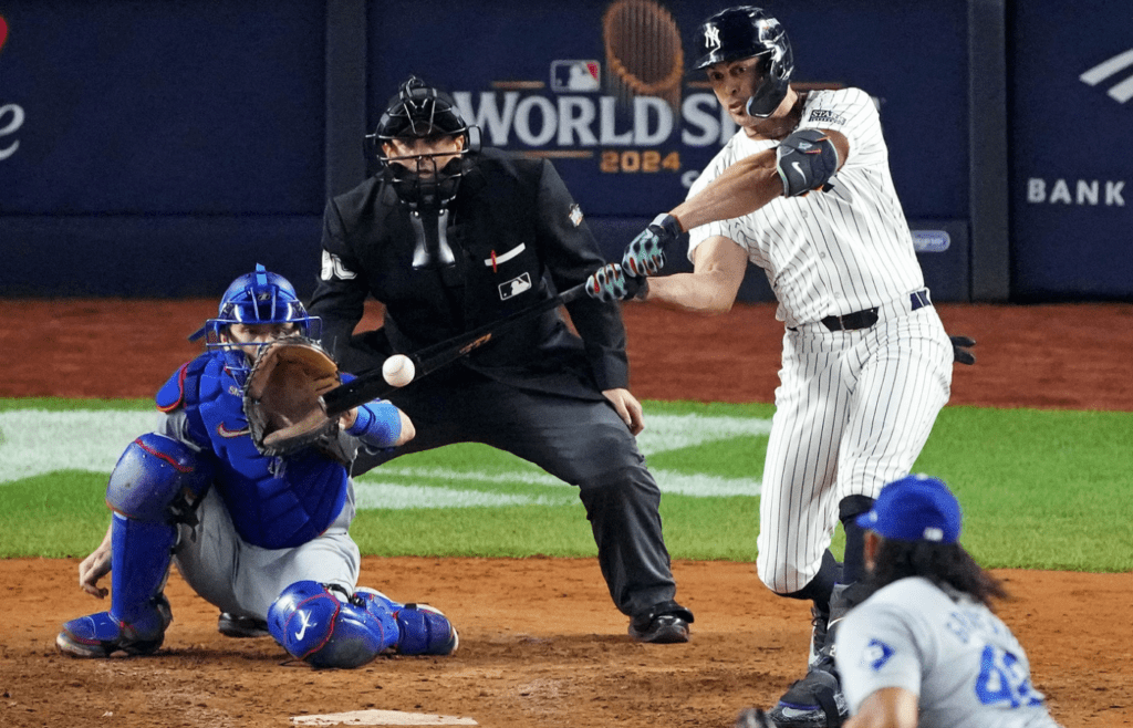 Oct 30, 2024; New York, New York, USA; New York Yankees designated hitter Giancarlo Stanton (27) hits an RBI sacrifice fly during the sixth inning against the Los Angeles Dodgers in game four of the 2024 MLB World Series at Yankee Stadium. Mandatory Credit: Robert Deutsch-Imagn Images