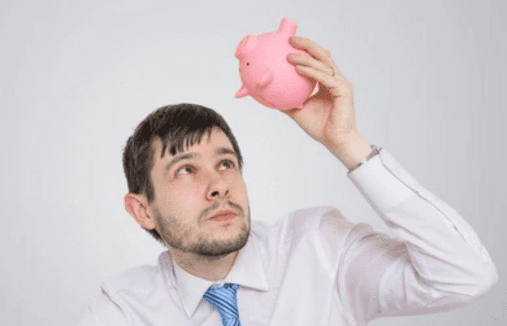 A young adult looking at an empty piggy bank