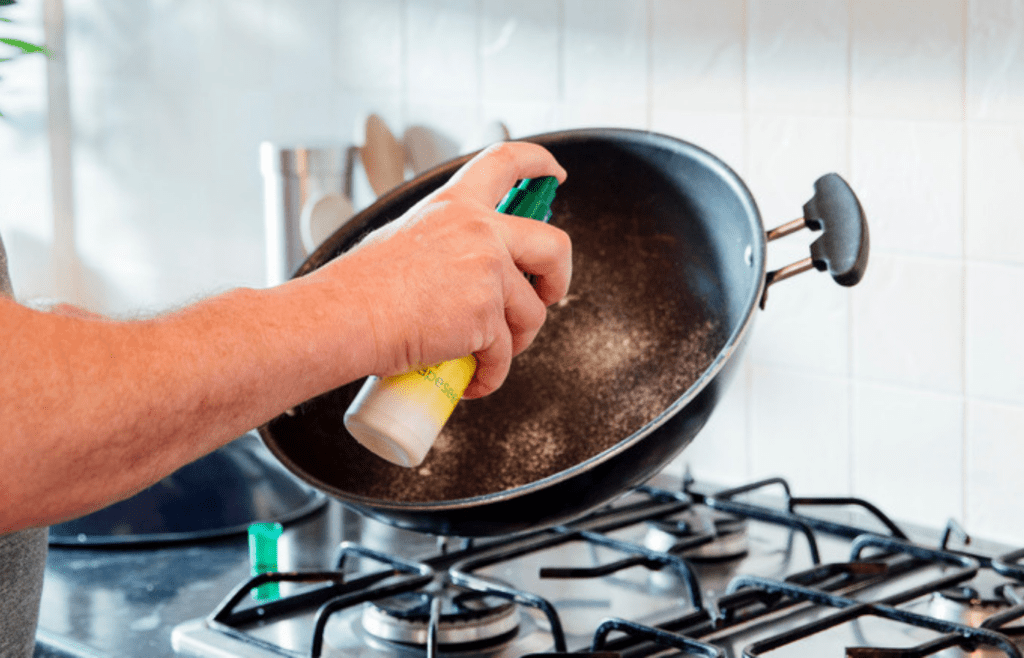 A hand spraying a nonstick pan