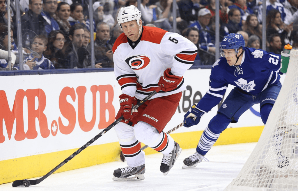 Dec 29, 2013; Toronto, Ontario, CAN; Carolina Hurricanes defenseman Mike Komisarek (5) with the puck as he is pursued by Toronto Maple Leafs left wing James van Riemsdyk (21) behind the net at Air Canada Centre. The Maple Leafs beat the Hurricanes 5-2. Mandatory Credit: Tom Szczerbowski-Imagn Images