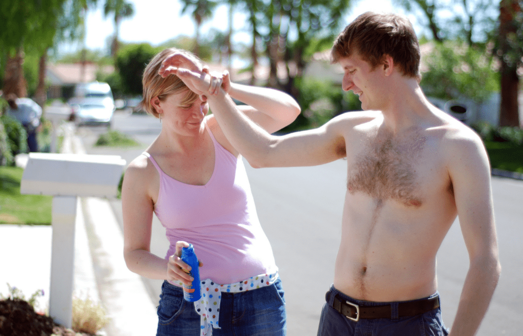 Woman spraying sunscreen on man’s arm