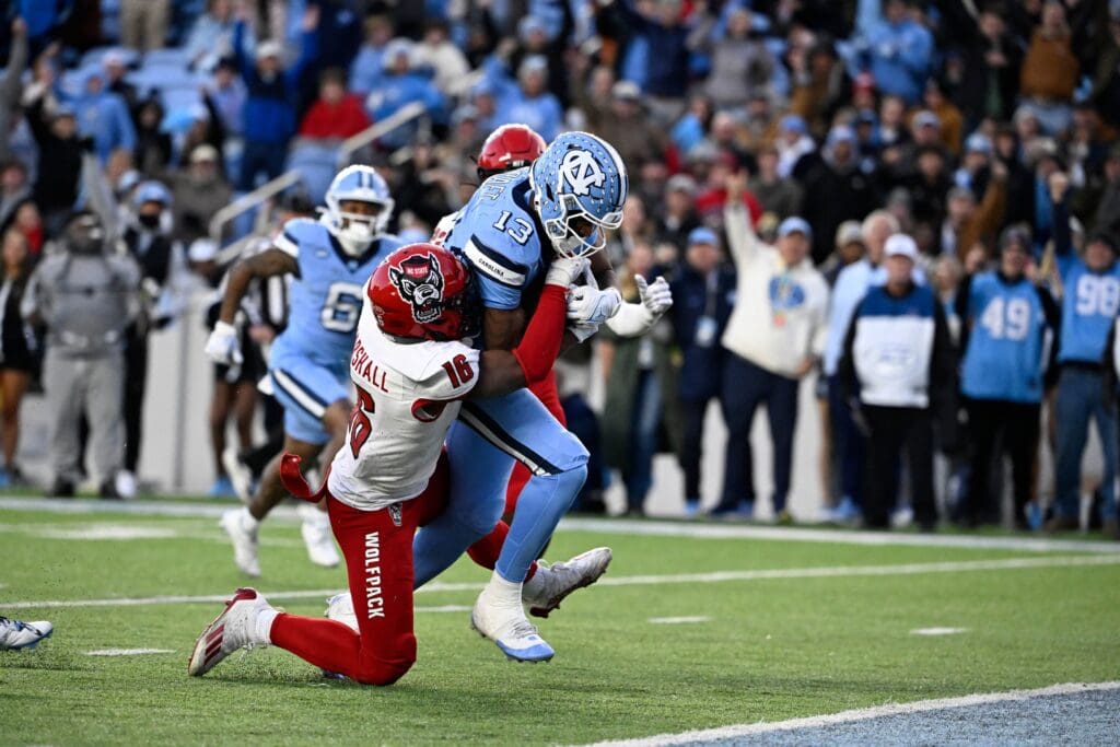 Nov 30, 2024; Chapel Hill, North Carolina, USA; North Carolina Tar Heels wide receiver J.J. Jones (13) scores a touchdown as North Carolina State Wolfpack cornerback Devon Marshall (16) defends in the second quarter at Kenan Memorial Stadium. Mandatory Credit: Bob Donnan-Imagn Images