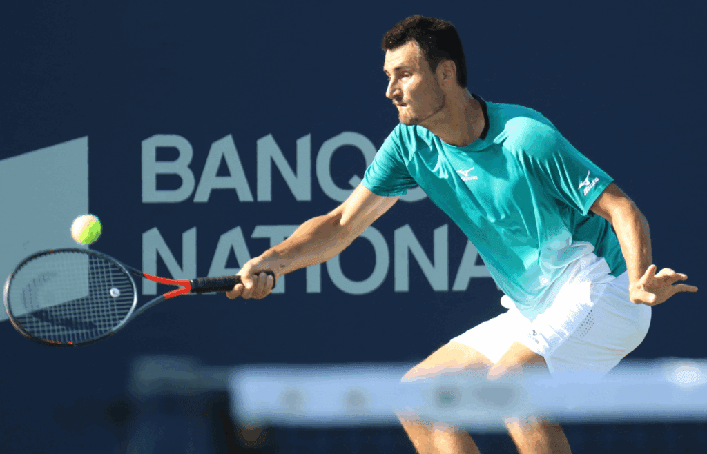 Aug 5, 2019; Montreal, Quebec, Canada; Bernard Tomic from Australia hits a shot against Roberto Bautista Agut from Spain (not pictured) during the Rogers Cup tennis tournament at Stade IGA. Mandatory Credit: Jean-Yves Ahern-Imagn Images