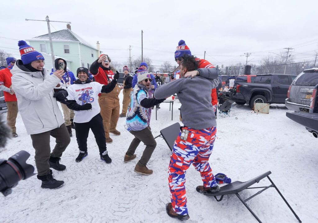 Colin Bhat, of the Bronx, gets congratulated by his friends after jumping and smashing a table in a parking lot where they were tailgating before the Buffalo Bills divisional game against the Baltimore Ravens at Highmark Stadium in Orchard Park on Jan. 19, 2025.