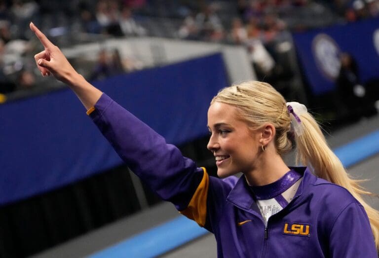 Mar 22, 2025; Birmingham AL, USA; LSU gymnast LSU gymnast Livvy Dunne walks with teammates to a competition area and gestures to fans during Session 2 of the SEC Gymnastics Championship at Legacy Arena in Birmingham, Alabama. LSU won the event to claim the SEC crown.