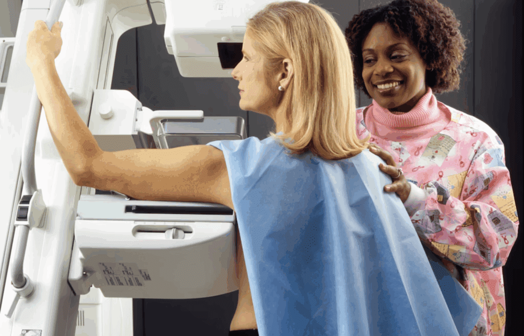 Smiling woman standing near another woman beside mammogram machine