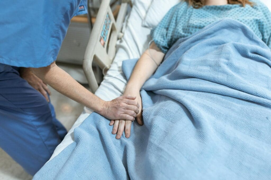 person in blue scrub holding patient's hand